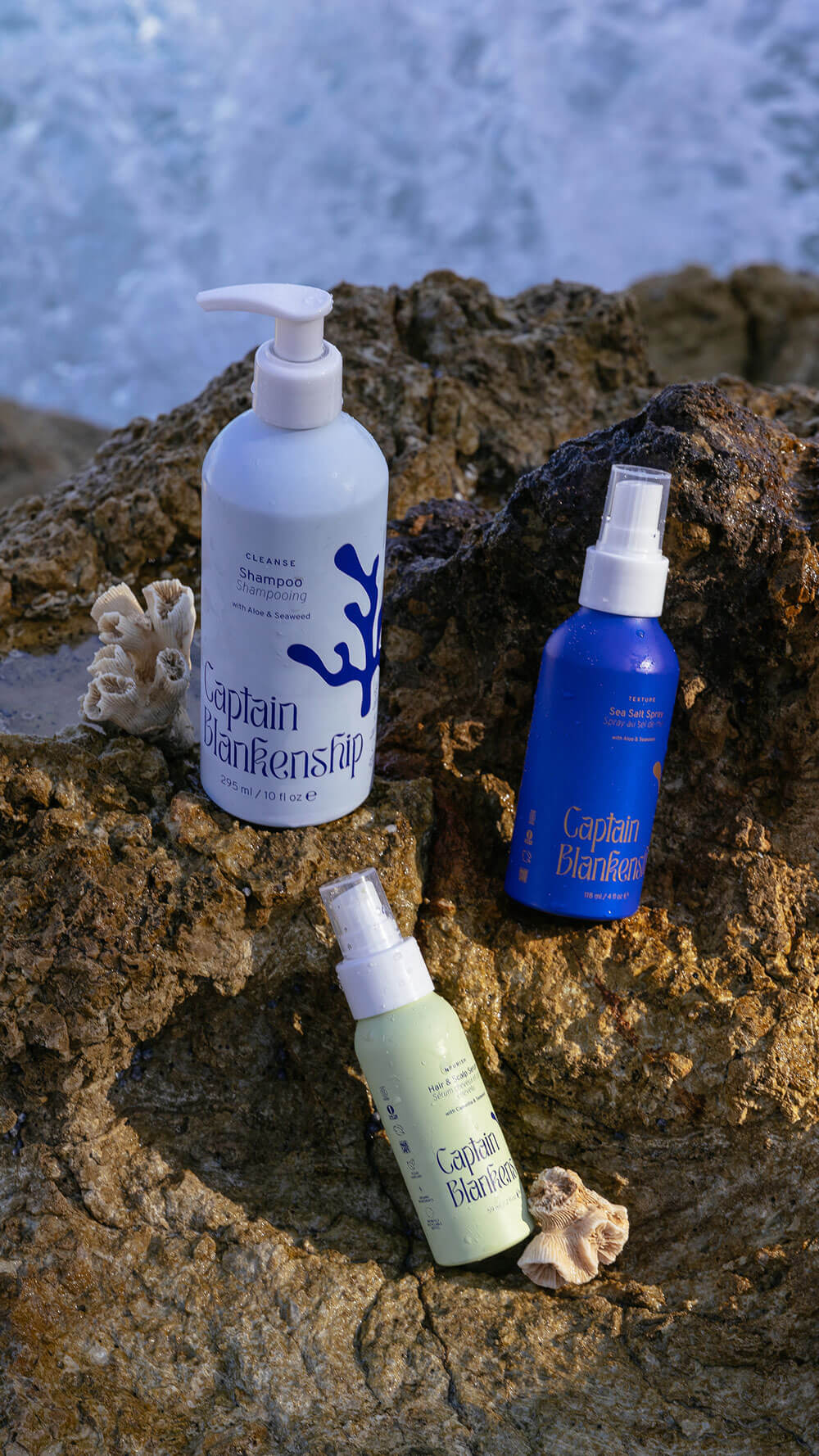 Captain Blankenship Hydrate Conditioner with Aloe and Shea Butter, Texture Sea Salt Spray with Aloe and Seaweed, and Nourish Hair and Scalp Serum with Argan and Camellia on a rock