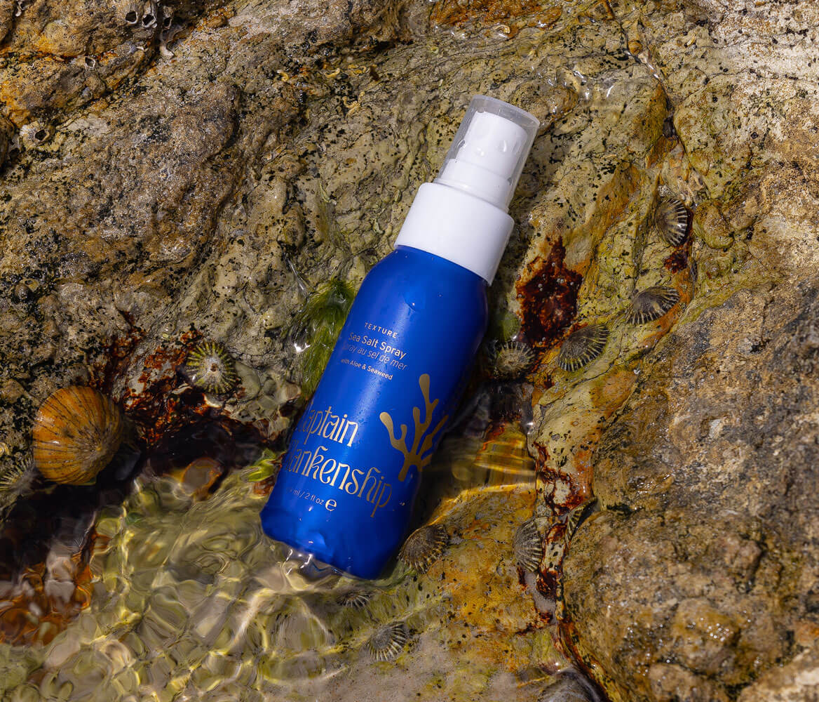 Texurizing sea salt hair spray with aloe and seaweed lay on a rock half submerged in water